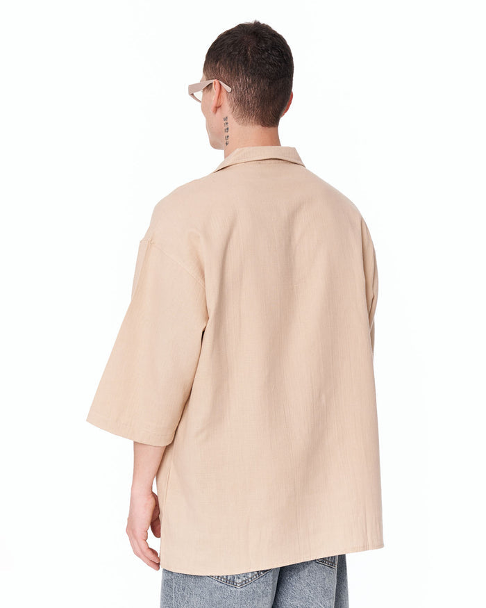Martin Valen oversized men's beige linen shirt, back three-quarter view showing drop shoulder and wide sleeves over light blue jeans