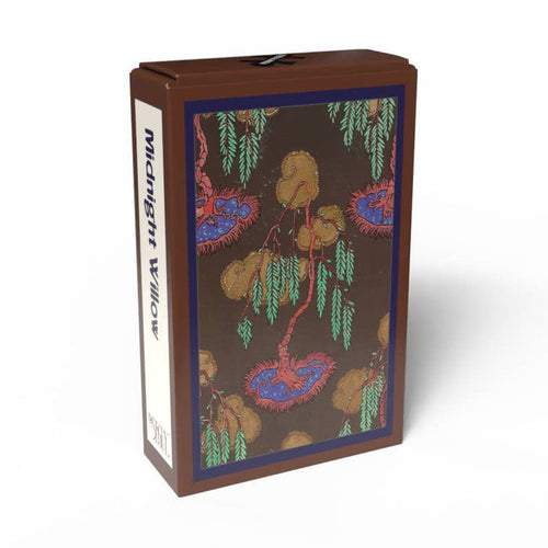 A brown rectangular box labeled “Midnight Willow” from Penny Puzzle, featuring a decorative illustration of willow trees on the front panel, captures the vintage charm of a 99-piece mini jigsaw puzzle and draws inspiration from Art Deco puzzle designs reminiscent of E. A. Séguy’s artistic style.