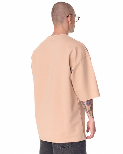 Martin Valen oversized beige T‑shirt in three‑quarter profile, chest logo visible and dropped shoulder sleeve