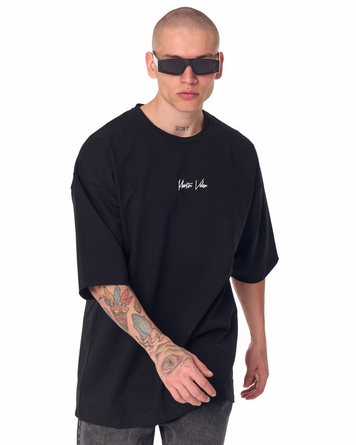 Martin Valen oversized black T‑shirt seen from back, wide shot showing right sleeve and tattooed forearm