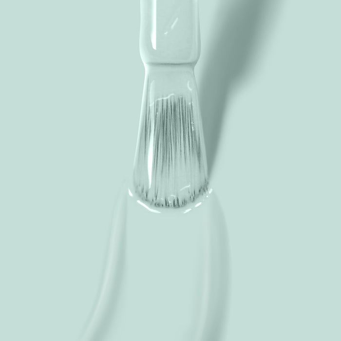 Close-up of a paintbrush dipped in LONDONTOWN's Mint No Chip paint against a light green background.
