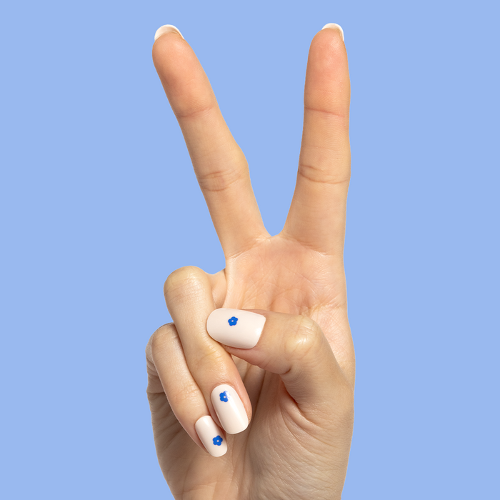 Mod Flowers | Short | Round - Tab Press-On nails with neutral polish and small modern blue floral accents on peace sign hand against blue background