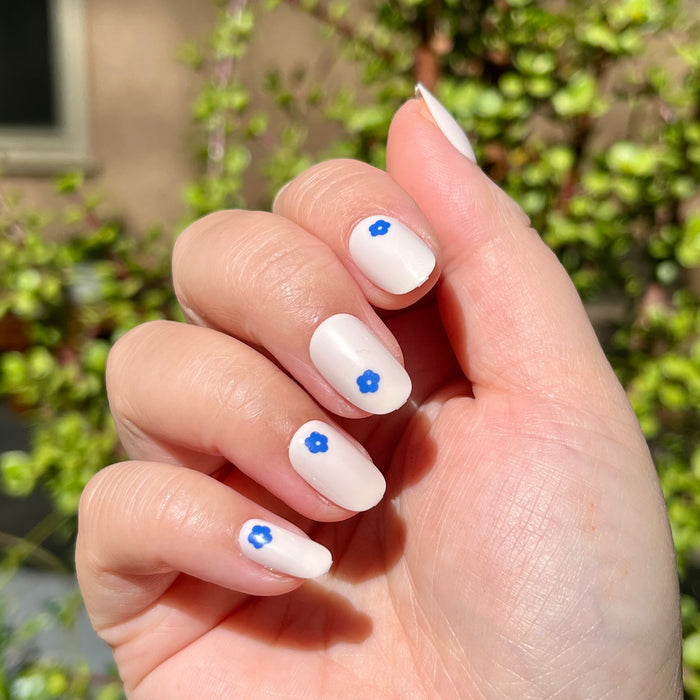 Mod Flowers | Short | Round - Tab Press-On nails with neutral polish and small blue floral accents on hand outdoors in sunlight