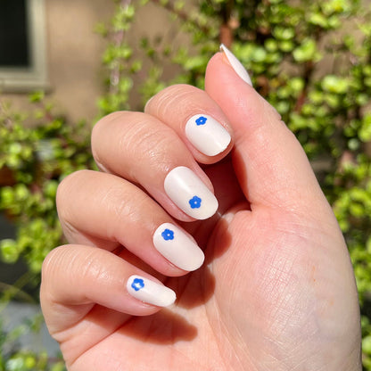 Mod Flowers | Short | Round - Tab Press-On nails with neutral polish and small blue floral accents on hand outdoors in sunlight