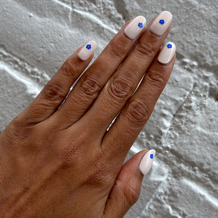 Mod Flowers | Short | Round - Tab Press-On nails with neutral polish and small modern blue flower accents on hand against textured gray background