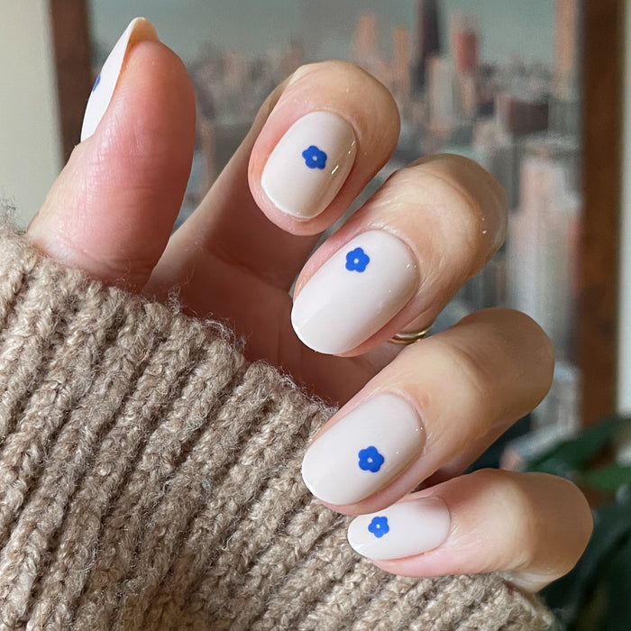 Mod Flowers | Short | Round - Tab Press-On nails with neutral base and small blue flower details on hand wearing cozy brown sweater