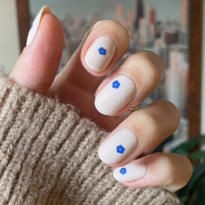 Mod Flowers | Short | Round - Tab Press-On nails with neutral base and small blue flower details on hand wearing cozy brown sweater