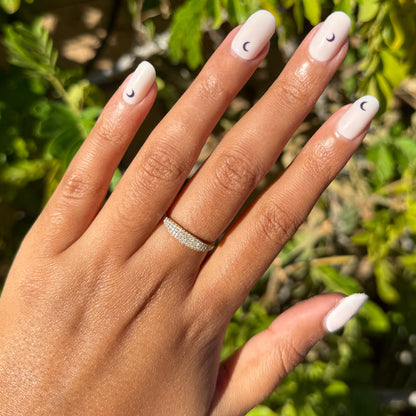 Moon Phases | Short | Squoval - Tab Press-On nails with pale neutral base and small dark crescent moon designs on hand outdoors