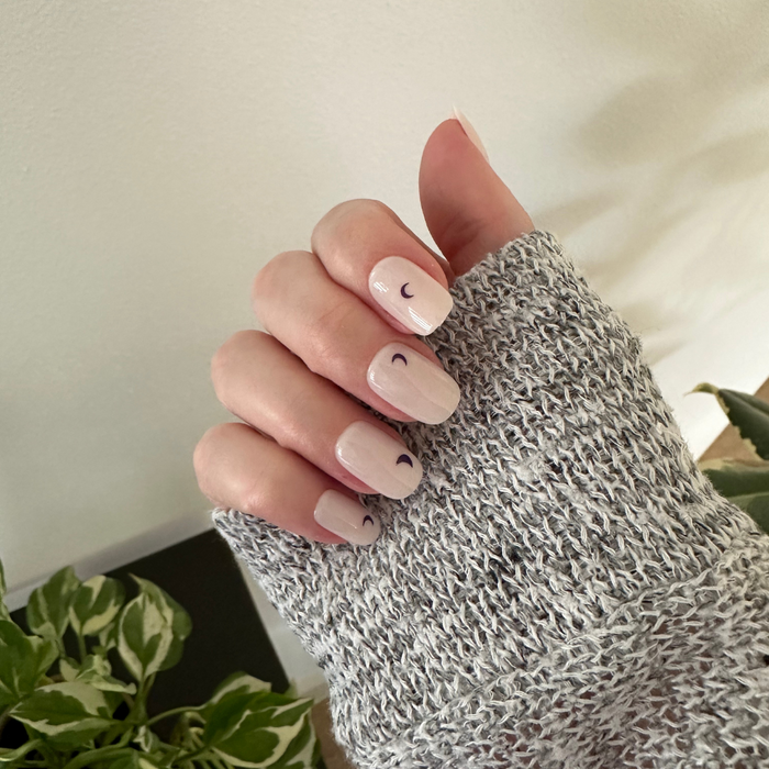 Moon Phases | Short | Squoval - Tab Press-On nails with light neutral base and small dark crescent moon designs on hand