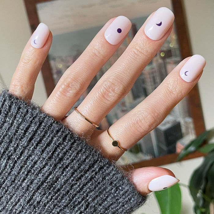 Moon Phases | Short | Squoval - Tab Press-On nails with pale base and small dark moon phase designs on hand indoors