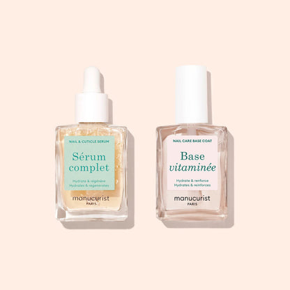 Two clear glass bottles with droppers—Manucurist Nail Moisturizing Duo—are set against a light beige background, designed to support healthy nails and deliver vitamin-rich hydration.