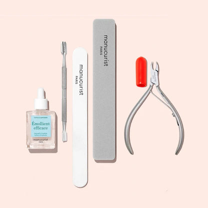 The Manucurist Ultimate Nail Prep Set includes a cuticle remover oil, metal cuticle pusher, emery board nail file, buffer, and stainless steel cuticle nippers with a red cap—all displayed on a light pink background.