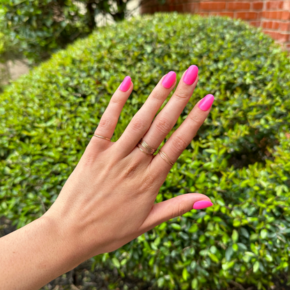 Neon Flamingo | Short | Round - Tab Press-On nails in bright true neon pink short round shape on hand outdoors with natural greenery background