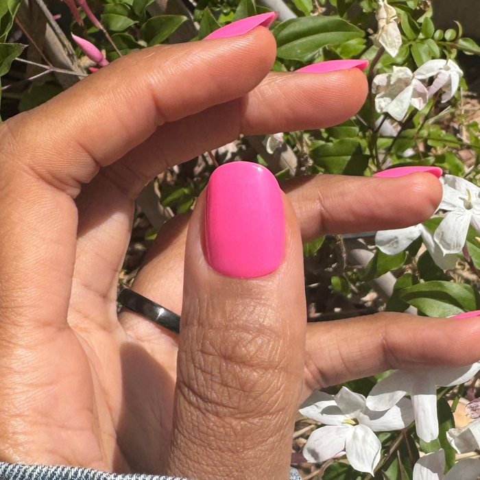Neon Flamingo | Short | Round - Tab Press-On nails in true neon pink on hand with natural white flowers in sunlight