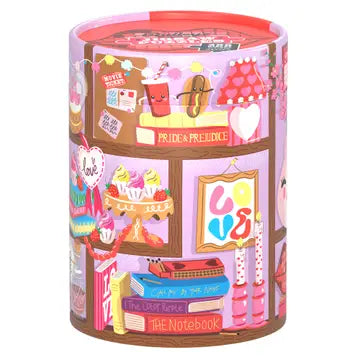 The “Objects of My Affection | 200 Piece Jigsaw Puzzle” by Chronicle Books comes in a colorful cylindrical container adorned with whimsical illustrations of books, cupcakes, and romantic-themed decorations set against a pink background. This delightful puzzle contains 200 pieces and is FSC certified.