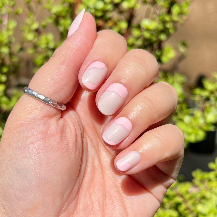 Organic Swirl | Extra Short | Round - Tab Press-On showing neutral nails with soft light pink swirl design on hand outdoors