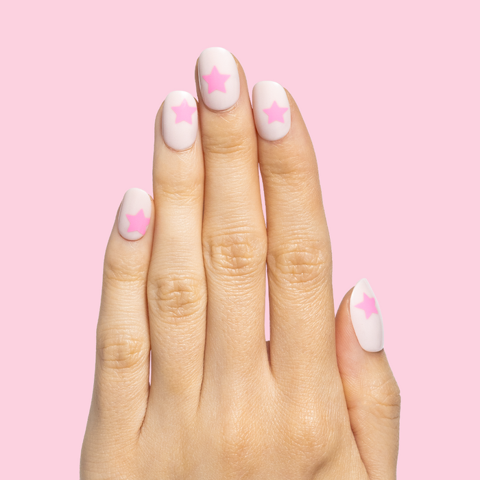Pink Star Party | Extra Short | Round - Tab Press-On nails with soft pink base and bright star accents on hand against pink background