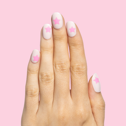 Pink Star Party | Extra Short | Round - Tab Press-On nails with soft pink base and bright star accents on hand against pink background