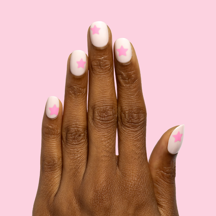 Pink Star Party | Extra Short | Round - Tab Press-On nails with soft pink base and vivid star design on hand over pink background