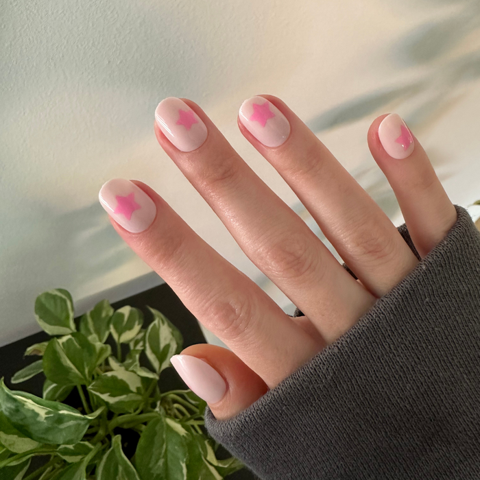 Pink Star Party | Extra Short | Round - Tab Press-On nails with soft pink base and translucent pink star accents on hand