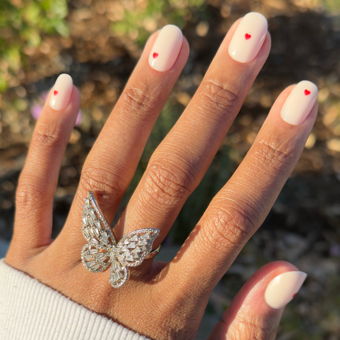 Hand with Red Hearts | Short | Round - Tab Press-On nails featuring neutral base and tiny red heart accents outdoors