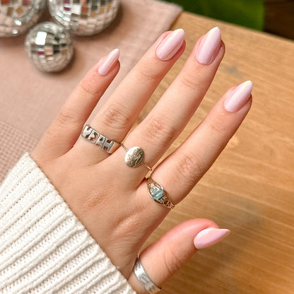 Hand with Rose Chrome - Press-On | Medium | Almond nails in glossy pink chrome finish wearing rings over light sweater on wood table