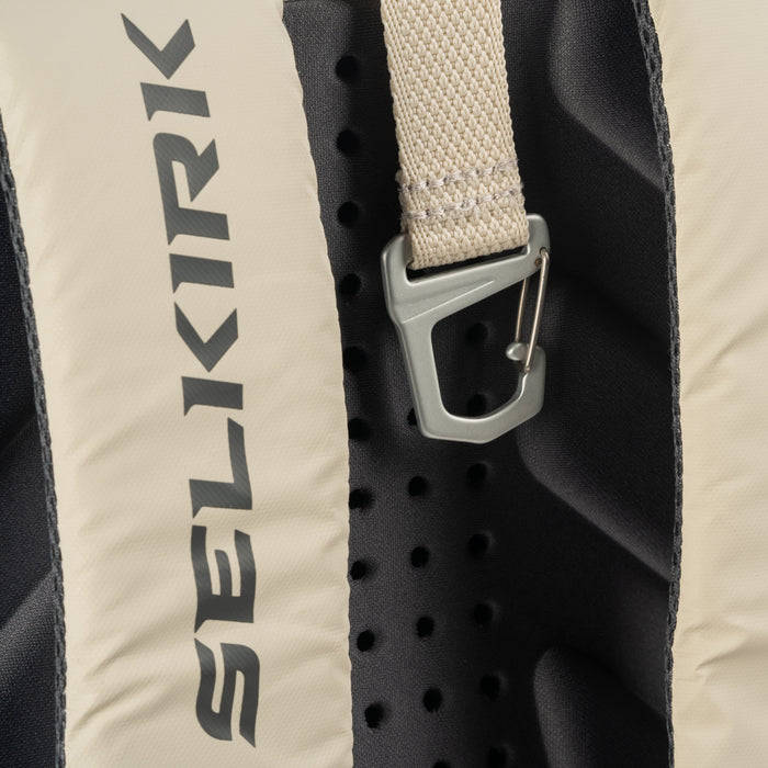 Vertical SELKIRK logo on beige backpack back panel, perforated black foam and metal strap clip.