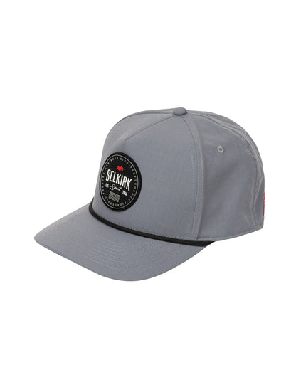 Gray six-panel baseball cap with round SELKIRK patch on front and black decorative cord along the brim