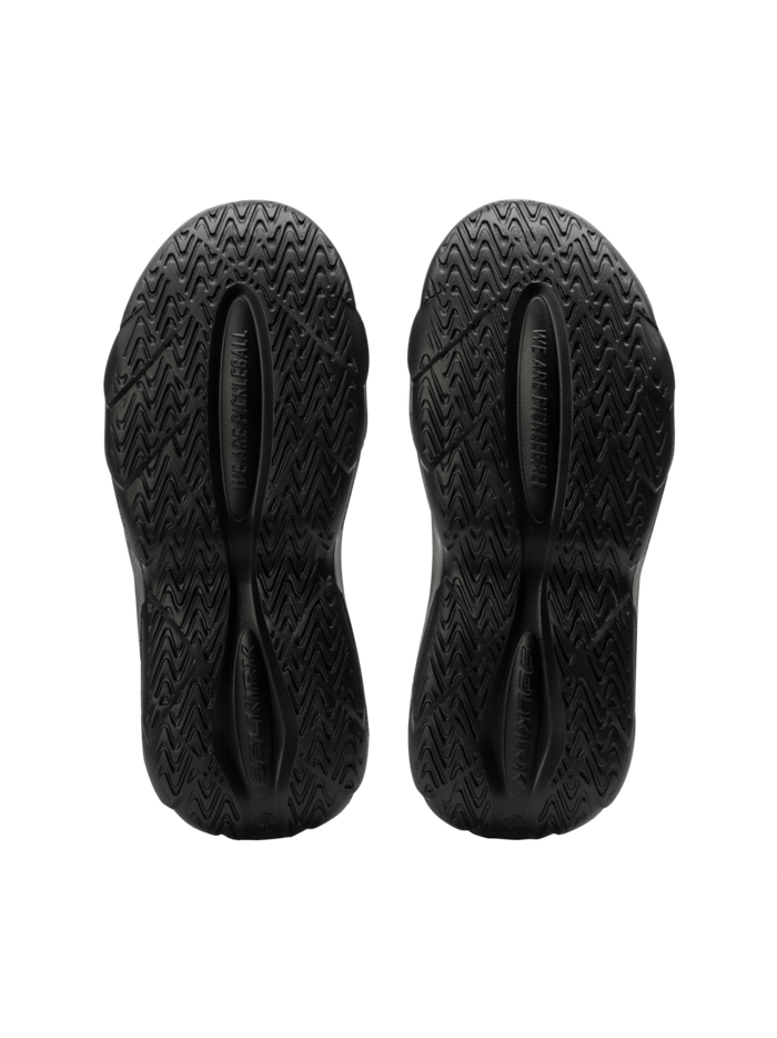 Bottom view of Selkirk Renew Pickleball Recovery Shoe showing black molded EVA outsoles with textured tread and ‘WE ARE HUMAN’ imprint