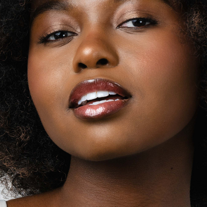Pink Lipps She’s All That Glow Lip Oil on lips of black model – high shine finish on medium to deep skin tone