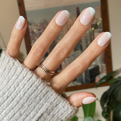 Side Swirl | Short | Round - Tab Press-On showing hand with neutral pink and white swirl press-on nails indoors with cozy knit sleeve