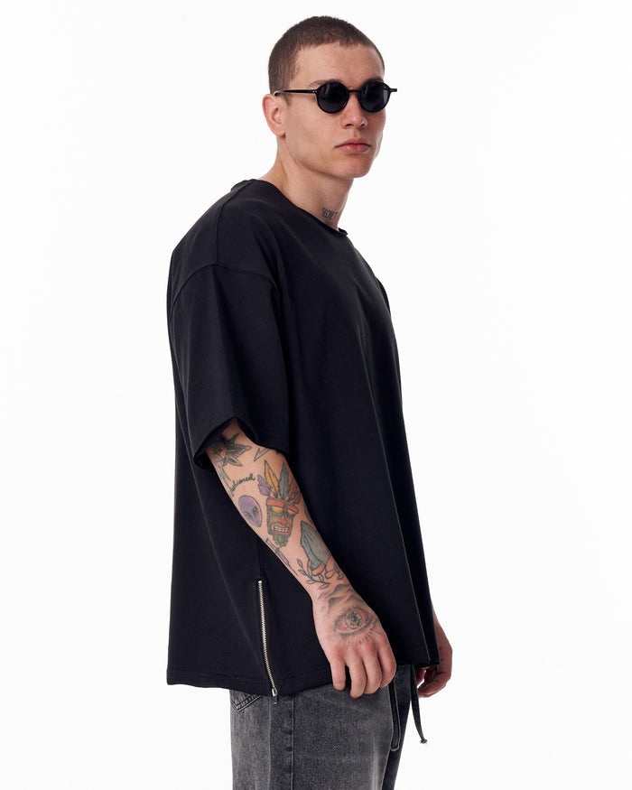 Martin Valen oversized black crew-neck T‑shirt, side view showing raw-edge neckline and visible side zipper at the hem