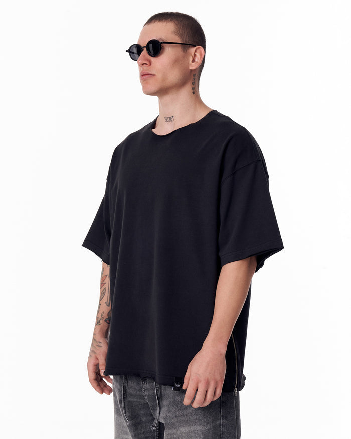 Martin Valen oversized black crew-neck T‑shirt, three-quarter view showing the side zipper detail and relaxed hem over jeans