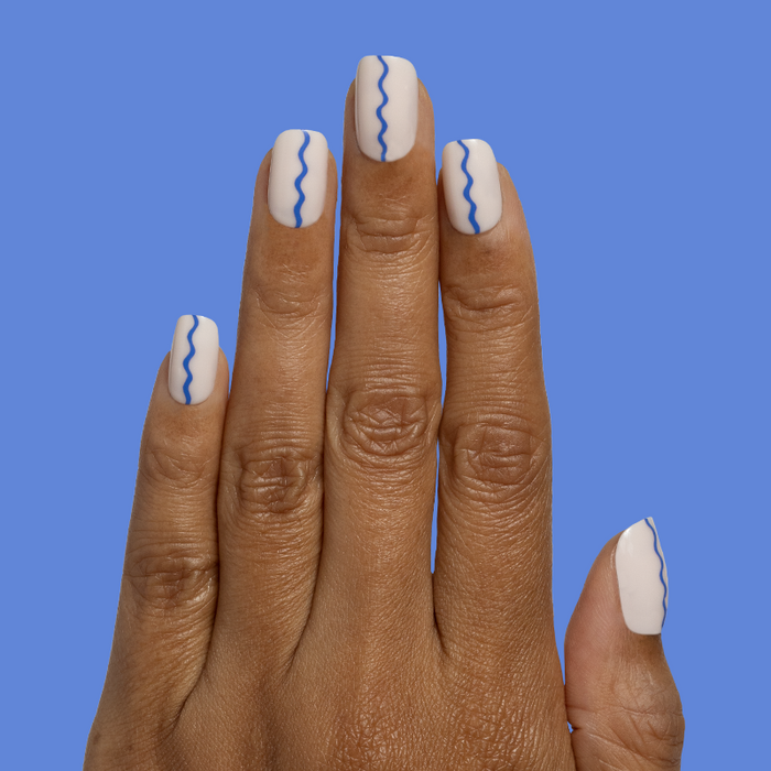 Simple Squiggle | Short | Squoval - Tab Press-On nails with neutral base and delicate blue wavy line mani on hand against blue backdrop