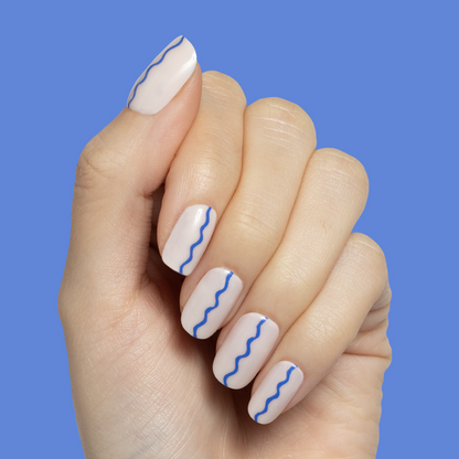 Simple Squiggle | Short | Squoval - Tab Press-On nails with neutral base and thin blue squiggle line on hand against blue background