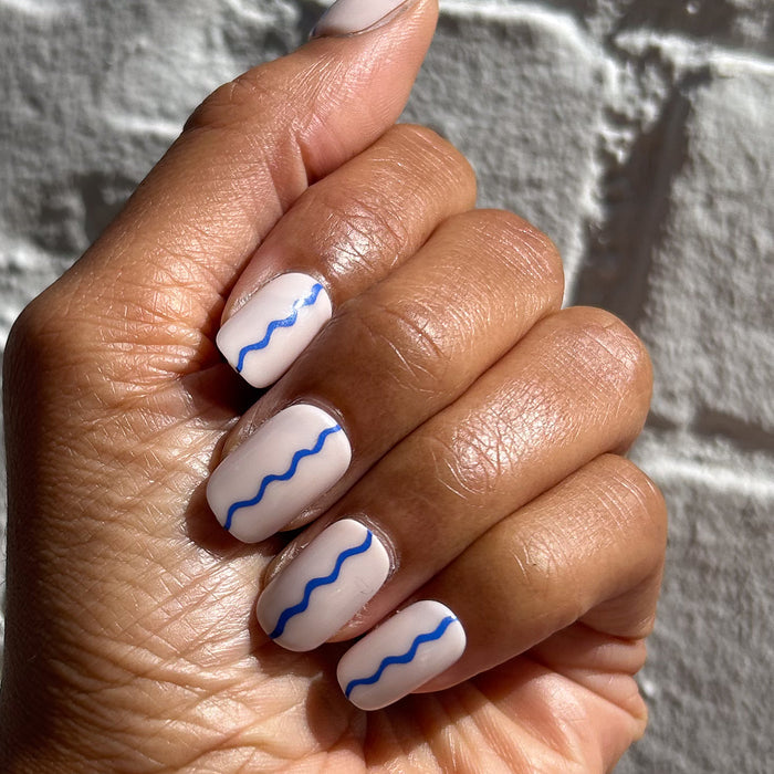 Simple Squiggle | Short | Squoval - Tab Press-On nails with white base and blue wavy line manicure on hand in sunlight
