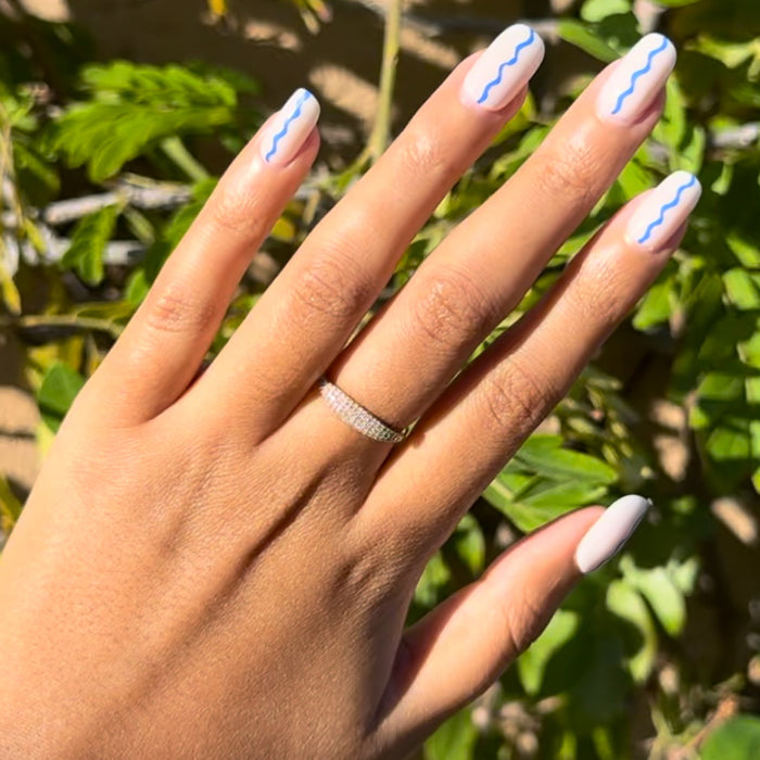 Simple Squiggle | Short | Squoval - Tab Press-On nails with neutral base and blue wavy line manicure on hand outdoors in sunlight