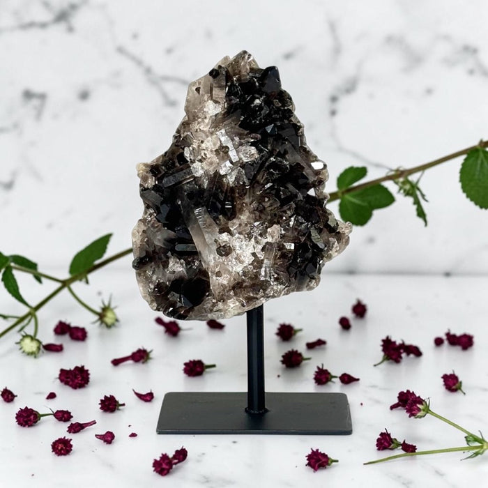 Smoky Quartz Cluster on Stand on a stand with flowers and leaves on a marble background