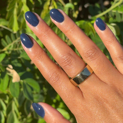 Suited - Gel smooth dark navy gel polish manicure on short natural nails shown on hand with green leafy background