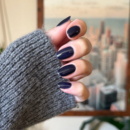 Suited - Gel deep navy gel polish manicure on medium length nails shown on hand wearing gray knit sleeve indoors