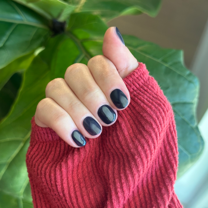 Suited - Gel deep dark navy gel polish manicure on short natural nails with hand partly covered by rust red sweater sleeve