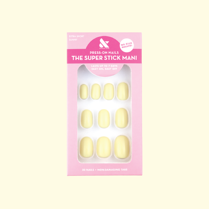 Sunny | Extra Short | Round - Tab Press-On nails in pastel yellow with non-damaging tabs in packaging on pale background