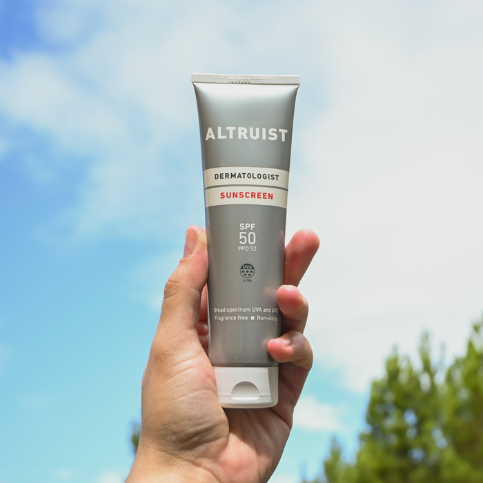 Hand holding a tube of Altruist sunscreen with a blue sky and trees in the background
