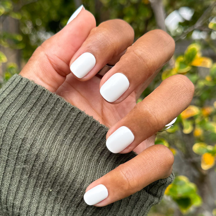 Swan | Extra Short | Squoval - Tab Press-On showing hand with crisp white nails outdoors against natural green background