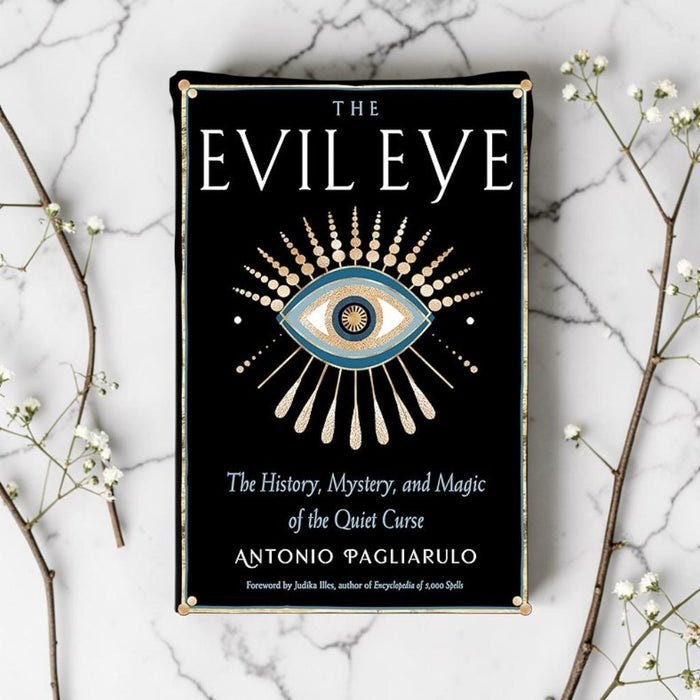 Book cover of 'The Evil Eye' on a marble surface with decorative branches.