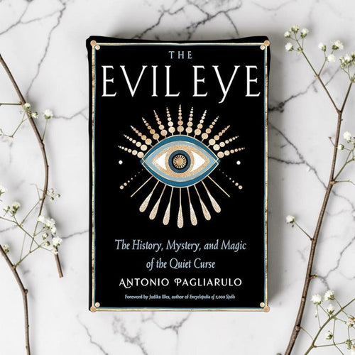 Book cover of 'The Evil Eye' on a marble surface with decorative branches.