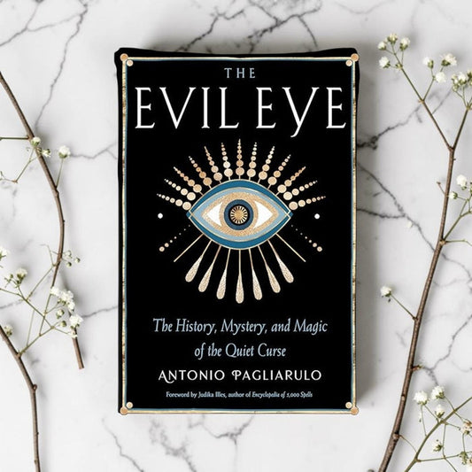 Book cover of 'The Evil Eye' on a marble surface with decorative branches.