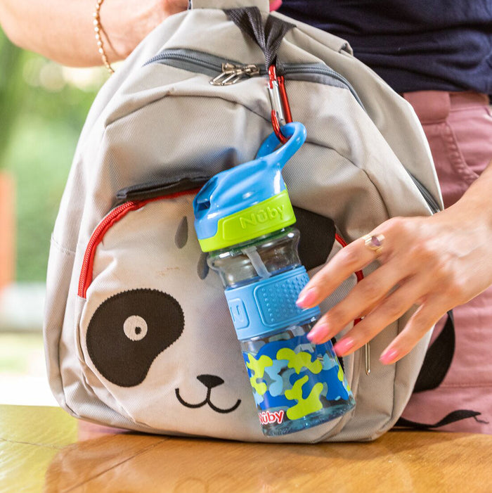 A person’s hand touches a gray backpack with a panda face. A Thirsty Kids REFLEX Easy Grip Water Bottle | Blue Camo is clipped to the bag’s zipper with a red carabiner.