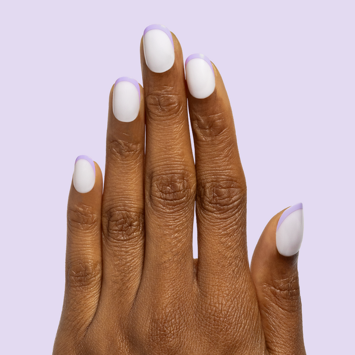 Tonal Lavender French | Extra Short | Round - Tab Press-On nails with white base and soft lavender tips on hand against pale lavender background