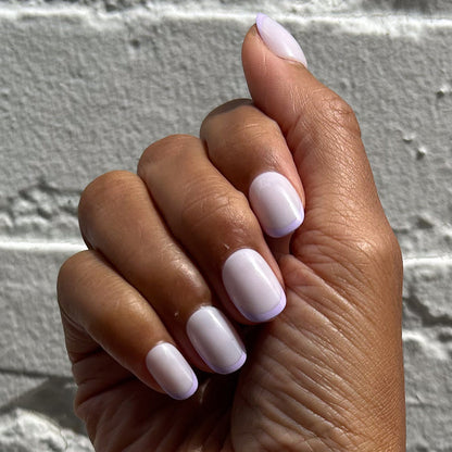 Tonal Lavender French | Extra Short | Round - Tab Press-On nails with soft lavender French tips on hand against textured white wall